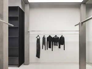 極簡服裝零售展示，黑色衣架上懸掛各式黑色服飾，置於金屬桿上。