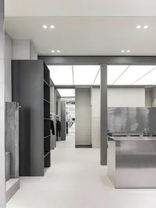 A sleek, minimalist clothing retail shop featuring concrete, metal, and glass materials.