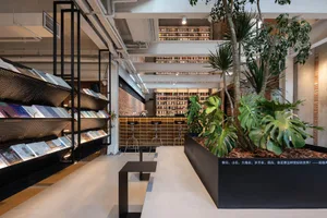 A modern bookstore cafe with metal shelves, brick walls, concrete flooring, and tropical plants.