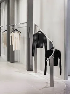 A modern retail clothing store displays minimalist clothing on metal hangers with a concrete and glass interior design.
