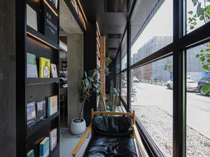 Interior view of a modern urban library with minimalist design, featuring black leather furniture, concrete walls, and large 