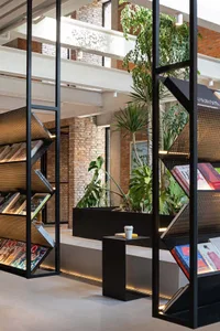 A modern industrial library interior with exposed concrete walls and metal shelves, featuring green plants for decoration.