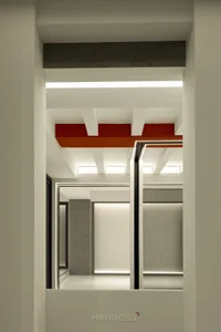 A modern office space featuring white concrete walls and floors with a vibrant red ceiling beam