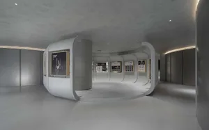 A minimalist exhibition suite featuring concrete walls and flooring, with various artworks and informational displays.
