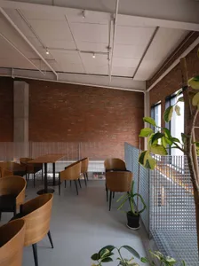 A spacious coffee shop with exposed brick walls, metal railings, and wooden furniture.