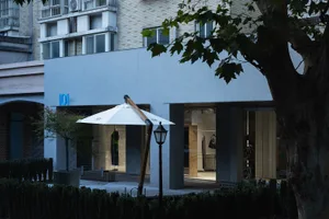 A modern retail storefront featuring a white parasol, wooden structure, and glass display windows.