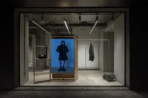 A retail storefront display features a digital screen with a model presenting fashionable clothing.