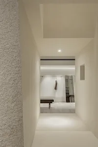 A minimalist room with concrete walls and floor, minimal furniture, and a single jacket hanging on the wall.