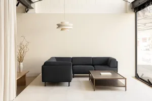 Contemporary living room with a black sectional sofa and a white pendant light hanging above, against a white wall.