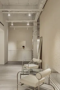 Contemporary waiting area with minimalist design featuring concrete walls and white leather chairs.