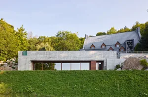 A modern residential house with a concrete exterior and a green hedge in the foreground.