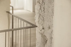 A close-up view of a stairway with a concrete wall featuring a textured, cracked surface and a metal railing.