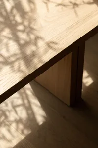 A minimalist wooden table with geometric腿 design, casting a shadow on the floor.