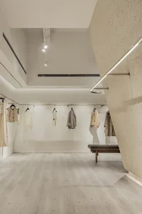 Modern retail store interior with minimalist design, neutral-toned materials, and clothing on display.