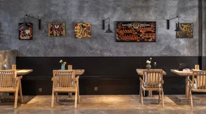 A cozy cafe interior with wooden chairs and concrete walls adorned with colorful art.