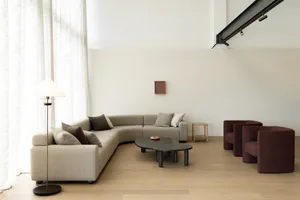 A modern minimalist living room with a wooden floor, a curved fabric sofa, and metal coffee tables.