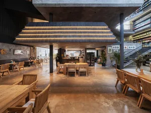 Well-lit industrial-style café interior with concrete flooring, wooden furniture, and bookshelves.