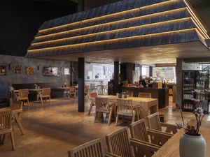 Modern industrial cafe interior with wooden tables, chairs, and concrete flooring.