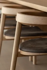 Three modern minimalist wooden chairs with brown leather seats.