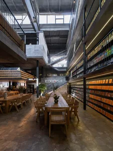 A spacious, industrial-style library and café with concrete walls, wood tables, and bookshelves filled with books.
