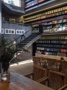A modern industrial library interior with wooden tables, metal railings, and glass shelves filled with books.