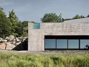 Concrete exterior of a modern minimalist house with large glass windows and a rock garden.