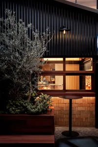 An exterior view of an industrial-style cafe featuring wood planters, brick walls, and metal accents.