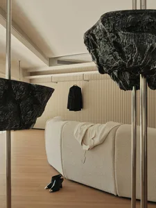 A minimalist living room with a sofa, black jacket hanging on the wall, and black shoes on the floor.