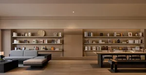 A modern library with wooden shelves containing books and decorative items. The floor is wooden, and there is a large sofa in