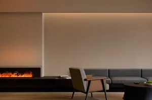 Modern living room with minimalist furniture, a grey sectional sofa, a brown armchair, and a fireplace with a warm ambient li