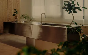 A contemporary kitchen interior features a sleek metal counter with a polished copper finish and a modern faucet.