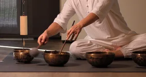 A person is seen using wooden mallets to strike metal bowls in a music therapy setting.