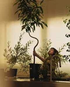 A woman gardening in a cozy indoor space surrounded by various plants and greenery.