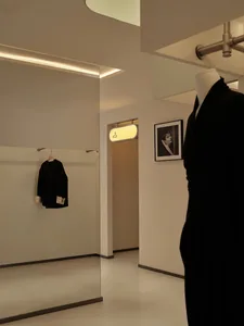 A minimalist clothing store interior with white walls, clothing racks, and a single dress on a mannequin.