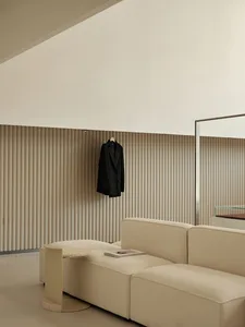 Minimalist living room featuring a beige sofa, plush cushions, vertical blinds, and a sleek mirror.