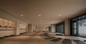 A spacious, minimalist yoga studio with wooden flooring, featuring yoga mats and cushions arranged in rows for practice.