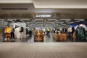 A modern retail storefront with concrete flooring, displaying And Wander clothing and accessories.