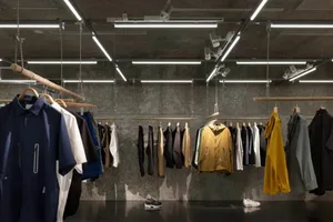 服飾店內金屬衣桿懸掛多款外套與襯衫，搭配混凝土背景牆。