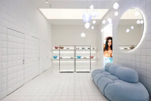 A minimalist retail space with white tiled walls and a blue fabric couch.