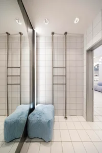 Modern bathroom interior with white ceramic tiles, minimalist design, and industrial-style metal ladders on the wall.