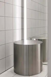 Modern minimalist bathroom featuring cylindrical metal stools on a white tiled floor and wall.
