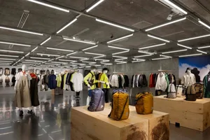 A modern retail space featuring clothing displayed on racks and mannequins, illuminated by linear lighting and a concrete cei