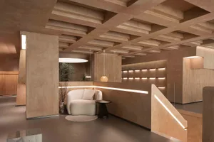A modern reception lounge featuring brownish concrete paneling, wooden ceiling beams, and warm lighting.