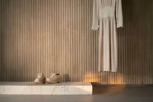 A minimalist fashion retail display featuring a white dress hanging on a corrugated wall and beige shoes on a marble platform