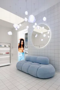 Modern fashion retail store with textured fiberglass cloud lights, white tiled walls, and blue cushioned bench seating.