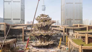 Construction site of a modern architectural structure with metal scaffolding and high-rise buildings in the background.