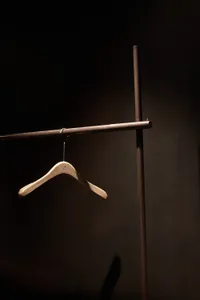A minimalist wooden clothing hanger suspended from a dark metal rod.