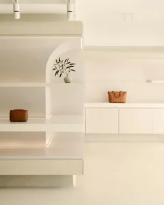A minimalist white display showcasing a vase and bags.