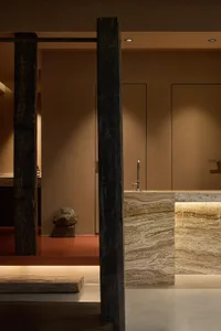 Modern bathroom interior with marble walls and countertop, wooden beams, and decorative rock.