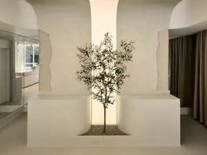 A minimalist interior space featuring a concrete tree planted in a square, illuminated niche.